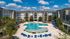 Luxurious apartment complex featuring a resort-style pool surrounded by sun loungers, modern buildings, and lush landscaping under a clear blue sky.