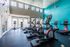 Modern fitness center with state-of-the-art cardio equipment, vibrant teal accent wall, and abundant natural light through large windows.