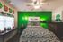 Vibrant bedroom with a striking green accent wall, modern chandelier, and artistic decor, creating a cozy and inviting atmosphere.
