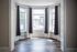 Elegant sunlit room with large bay windows, rich hardwood floors, and charming white detailing.