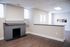 Bright and spacious living area with elegant wood flooring, featuring a stylish painted fireplace and ample natural light from large windows.