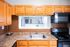 Charming kitchen view with sleek appliances, warm wooden cabinetry, and an inviting passthrough window to a bright living area.