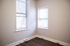 Bright corner room with sleek hardwood flooring and large windows draped in modern blinds, offering abundant natural light.