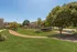 Welcoming green space in a residential community with lush lawns, mature trees, and walking paths under a clear blue sky.
