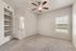 Bright and airy bedroom with plush carpeting, ceiling fan, built-in shelving, and a window offering scenic outdoor views.