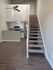 Modern apartment interior with elegant staircase leading to a lofted area, featuring an open-concept kitchen and living space with stylish lighting.