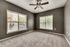 Bright and spacious room with large windows and plush carpeting, featuring modern ceiling fan.