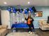 Cheerful event space with festive blue and silver balloon decor, a vibrant snack table, and a smiling guest holding treats, creating an inviting atmosphere.
