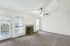 Bright living room with plush carpet, ceiling fan, and a cozy fireplace, featuring large windows and a balcony view.