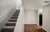 Sleek apartment entryway featuring a modern staircase with plush carpeting and elegant wood flooring leading to a stylish kitchen area.