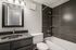 Elegant bathroom with modern fixtures, featuring a sleek black vanity, sparkling countertop, and stylish dark tile bathtub surround.
