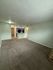 Spacious living area with plush carpeting, open sightlines to a modern kitchen, and ambient lighting for a cozy feel.