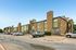 Charming apartment complex with brick exterior and modern green paneling, featuring ample parking space under a clear blue sky.