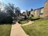 Charming apartment complex with beautifully landscaped green lawns, manicured shrubs, and a serene walkway in a sunlit, tranquil environment.