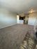 Inviting living room with plush carpet and cozy brick hearth, leading to an open kitchen with modern lighting.