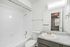 Bright and modern bathroom featuring a sleek granite countertop, spacious mirror, and pristine bathtub, with a glimpse into a well-lit adjoining bedroom.