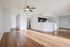 Bright and airy open-concept living space with sleek hardwood floors, showcasing a modern kitchen with dark cabinets and a cozy ceiling fan.