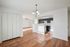 Bright open kitchen with modern black cabinetry and wood flooring, flowing into a sunlit living area with ceiling fan.