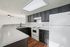 Modern kitchen with sleek dark cabinets, white countertops, and wood flooring, offering ample space and style.