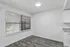 Bright modern kitchen space with sleek gray flooring, large window with blinds, and elegant white cabinetry.