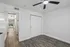 Bright and airy room with modern ceiling fan, sleek wooden floors, and minimalistic closet doors leading to a sunlit hallway view.