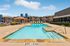 Inviting outdoor pool area at an apartment complex featuring a sparkling pool, ample sun loungers, and a charming wooden pergola, surrounded by modern architecture and lush landscaping.
