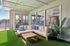 Chic indoor patio featuring a cozy L-shaped sofa with vibrant cushions, elegant wooden coffee table, lush artificial grass flooring, and expansive glass windows offering serene outdoor views.