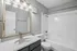 Spacious bathroom featuring a sleek vanity with a large mirror, bright lighting, and a pristine bathtub with modern fixtures.