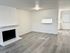 Bright open living area with modern flooring and a white brick fireplace, leading to a kitchen space.