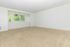 Sunny empty room with large windows and lush green views.