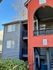 Charming apartment building exterior with a vibrant red entrance and modern blue siding, surrounded by lush greenery.