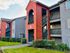 Charming apartment complex with vibrant red and grey exteriors, featuring lush greenery and inviting pathways.