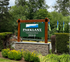 Inviting Parklane Townhomes entrance sign framed by lush greenery and vibrant flags.