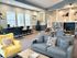 Inviting living space with modern seating, natural light from large windows, and a cozy reading nook with bookshelves.