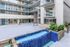 Modern apartment complex exterior with sleek balconies, vibrant blue water feature, and lush greenery enhancing the inviting atmosphere.