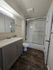 Elegant bathroom with modern gray vanity, sleek mirror, and pristine shower with glass doors, complemented by stylish dark wood flooring.