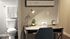 Compact Centennial Village bedroom home office with modern desk lamp and view of the bathroom featuring white towels and minimalistic d&eacute;cor.