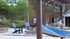 Centennial Village outdoor patio with a blue hammock, wooden pergola, and comfortable chairs, set against a backdrop of greenery and brick architecture.