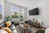 Bright and modern living room featuring a sleek black sofa, large flat-screen TV, and elegant decor, bathed in natural light from expansive windows.