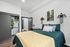 Cozy bedroom featuring a plush bed with green comforter and decorative pillows, stylish geometric wall shelves with plants, and an open closet displaying sports apparel.