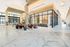 Spacious lobby with high ceilings, white marble floors, and modern chandeliers of interlinking rings. There is a colorful seating area in the foreground, two long working desks in the background, and a leasing desk and office behind a glass wall.