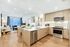Open-concept apartment kitchen, living, and dining space with light wood-style floors, a spacious living room with a large window, built-in shelves, light-colored frameless wood kitchen cabinets, white quartz countertops with an undermount sink, and stainless steel appliances.