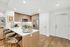 Apartment kitchen with light-colored wood cabinets and wood-style floors, white quartz countertops, a peninsula with three bar stools, stainless steel appliances, and white walls.
