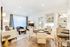 Open-concept living and dining area with a 4-person dining table, built-in desk, dry bar, and shelves, and a spacious living room with a large couch, armchair, media console, and coffee table.