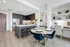 Open-concept kitchen and dining space with light ash-colored wood-style floors, dark cabinets, dry bar, dining table with 4 chairs, and a built-in desk with shelves and a chair.