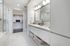 Spacious bathroom with a dual vanity with a white quartz countertop, walk-in closet, white marble tiling, and glass walk-in shower.