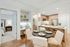 Open-concept apartment kitchen and dining space with a 4-person round dining table, light wood-style floors, a built-in desk and a dry bar with shelves, and an open door to a carpeted bedroom.