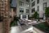 A landscaped stone courtyard with a large rectangular fire pit, 3 armchairs on each side, and an HDTV mounted on a freestanding stone wall.