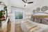 A spacious bedroom with a king-sized bed, ceiling fan, wood-style floors and large window.