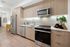 Studio apartment kitchen with stainless-steel appliances, modern light wood cabinetry, light wood-style floors and a tile backsplash.